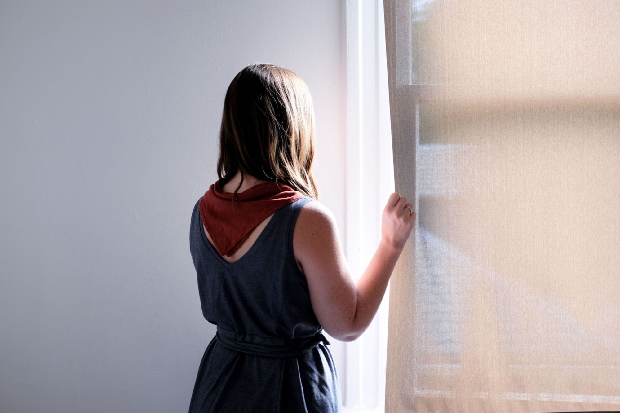 Alyssa is looking out the window. She is wearing a bandana and a blue dress from wool&