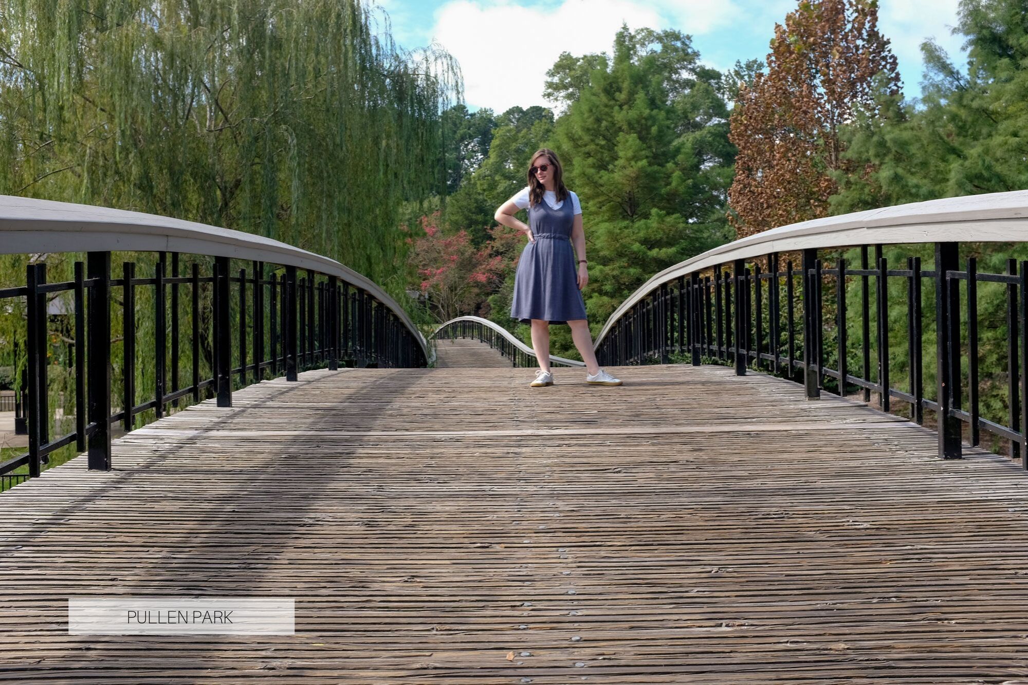 Krystal standing on a bridge in Pullen Park. There are lots of willow and flowering trees in the background