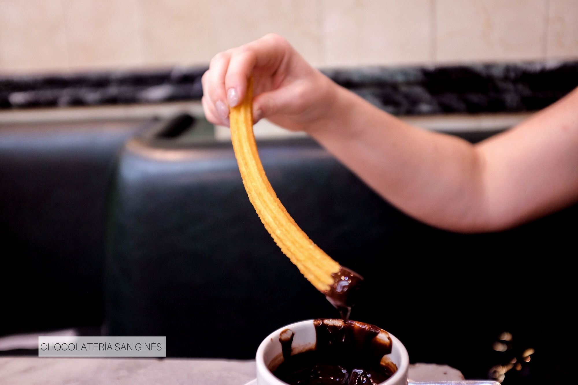 Alyssa's hand dunking a churro in a cup of chocolate at Chocolatería San Ginés