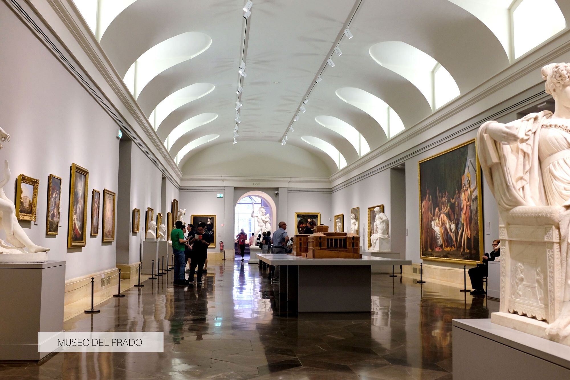 interior of a room in the Museo del Prado; there are paintings on the walls and sculptures along the center of the hallway.