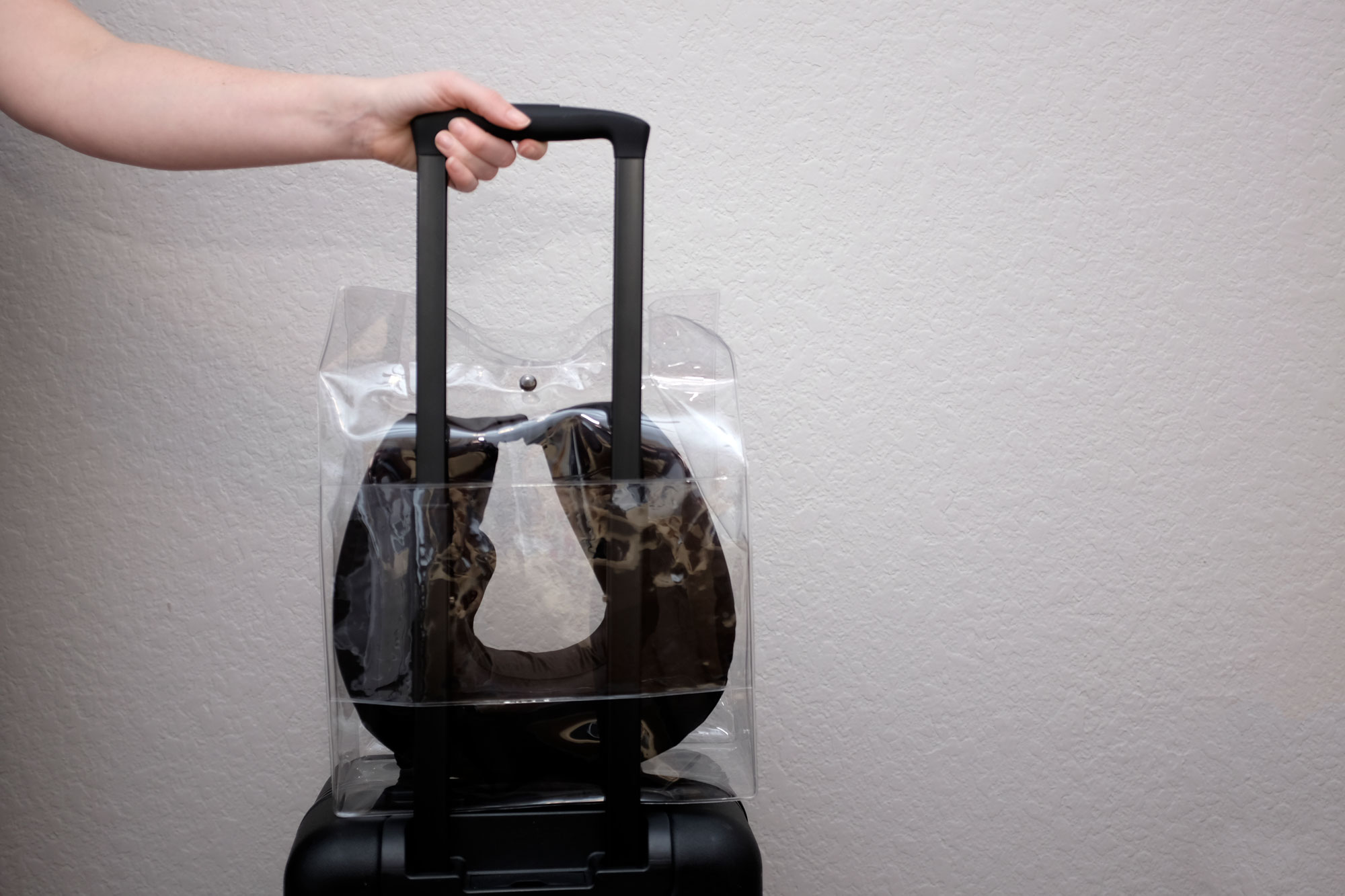 Alyssa's hand on the handle of her suitcase. The clear carrying case has been placed over the straps and is sitting on top of the suitcase.