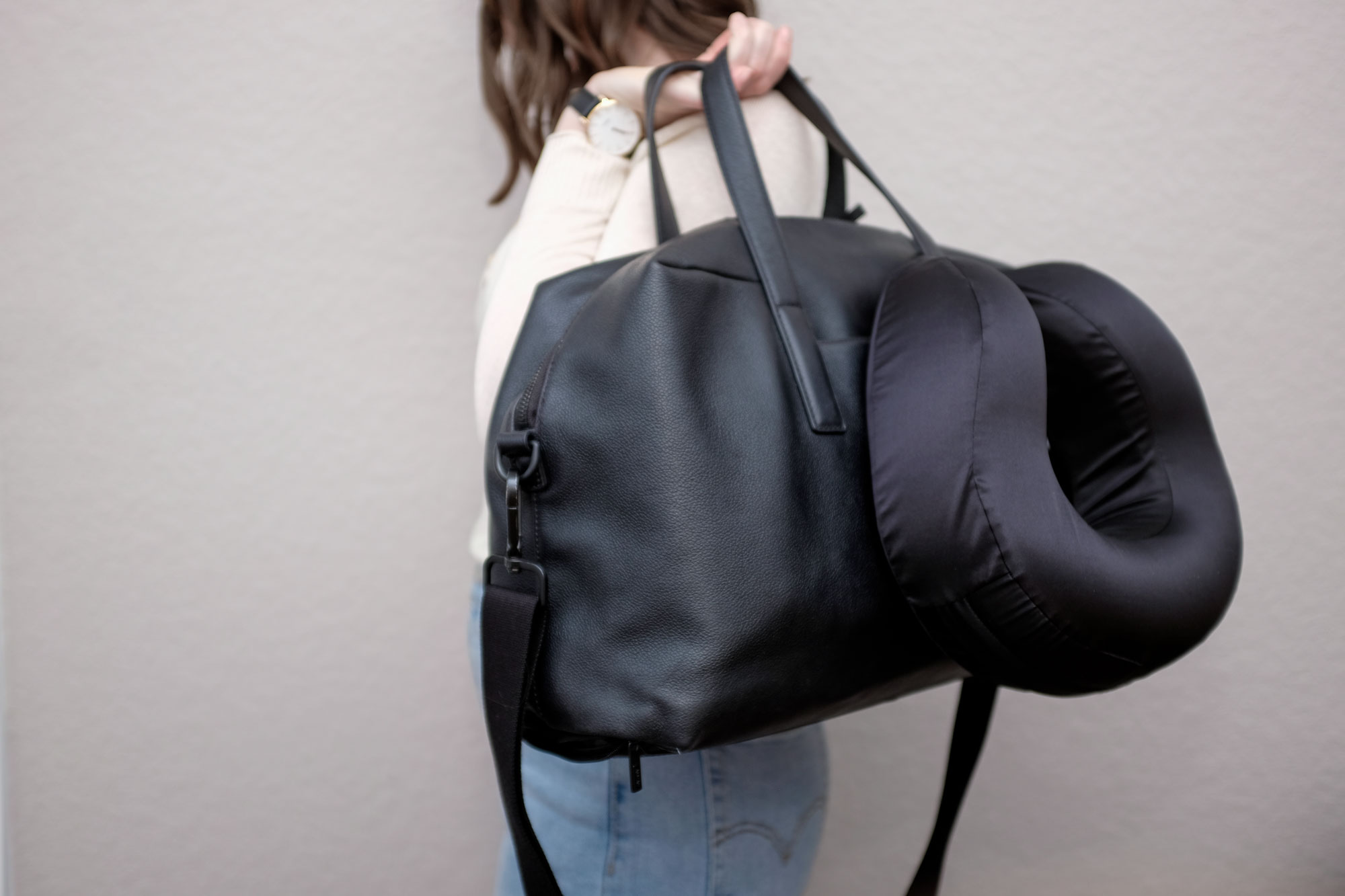 Alyssa holding a leather travel bag with the black silk pillow snapped on the exterior