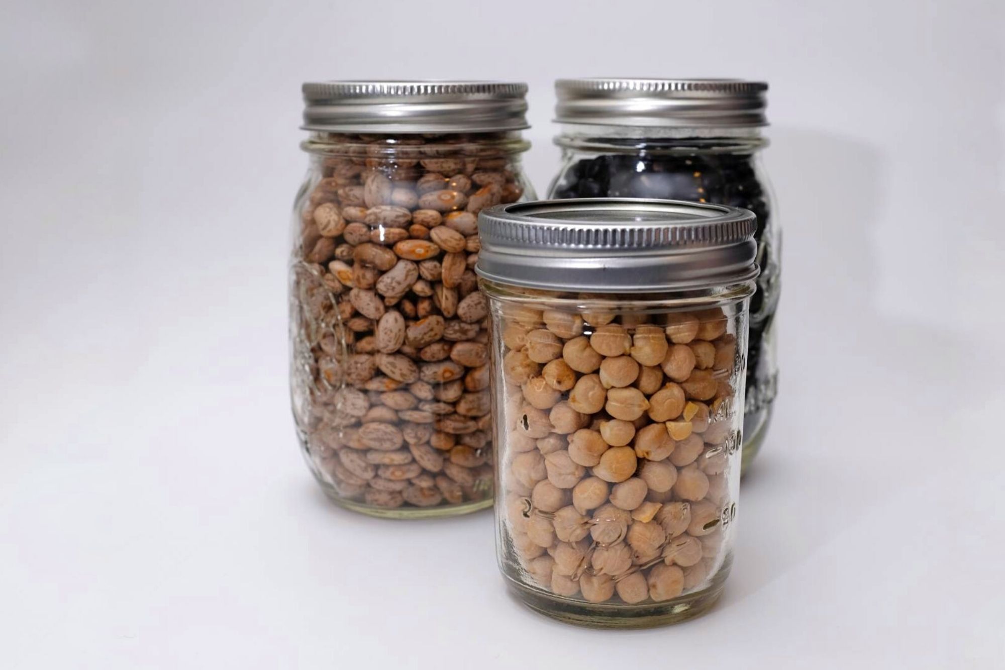 three mason jars with pinto beans, chickpeas, and black beans