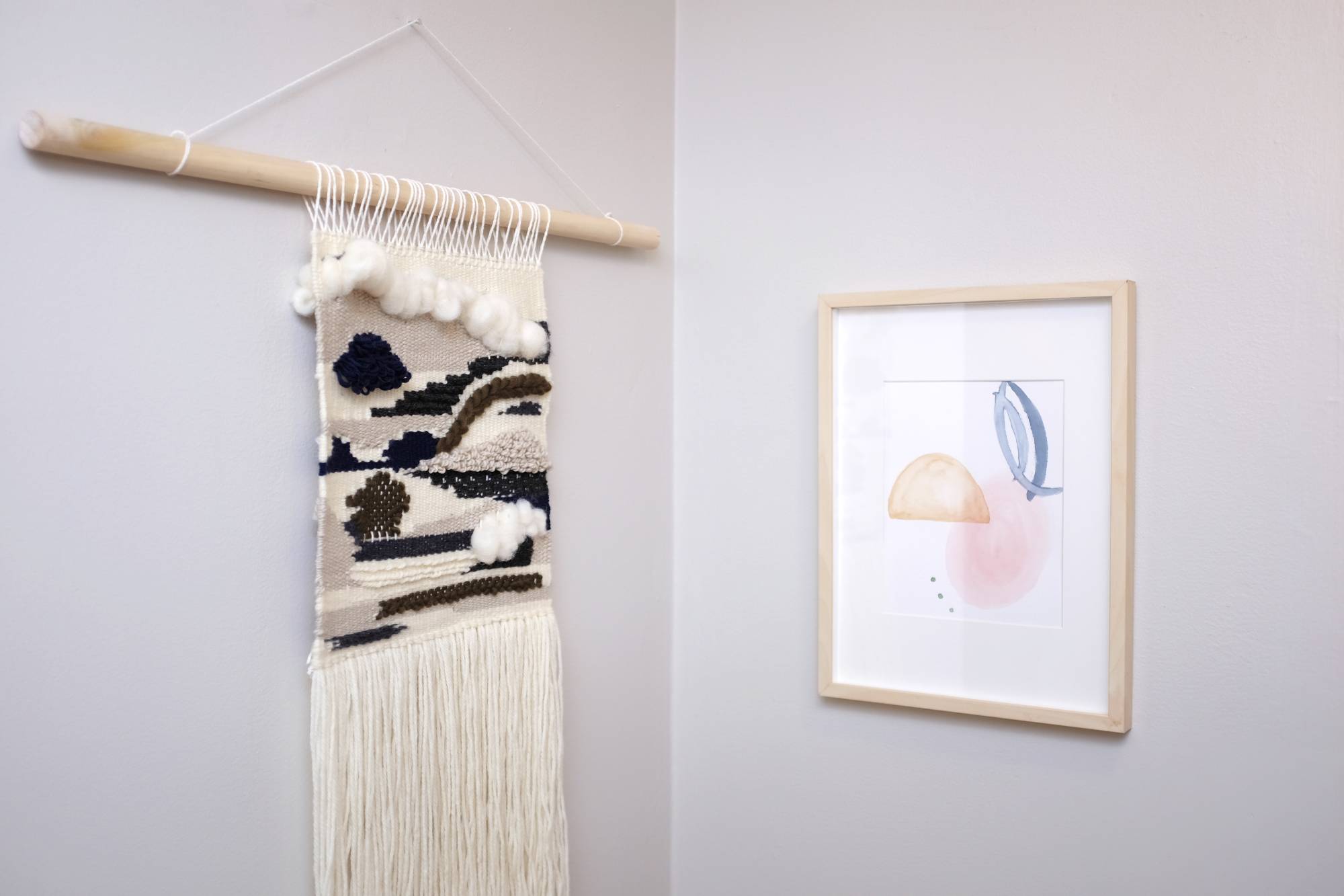 A weaving and a watercolor painting hung together in the corner of a hallway
