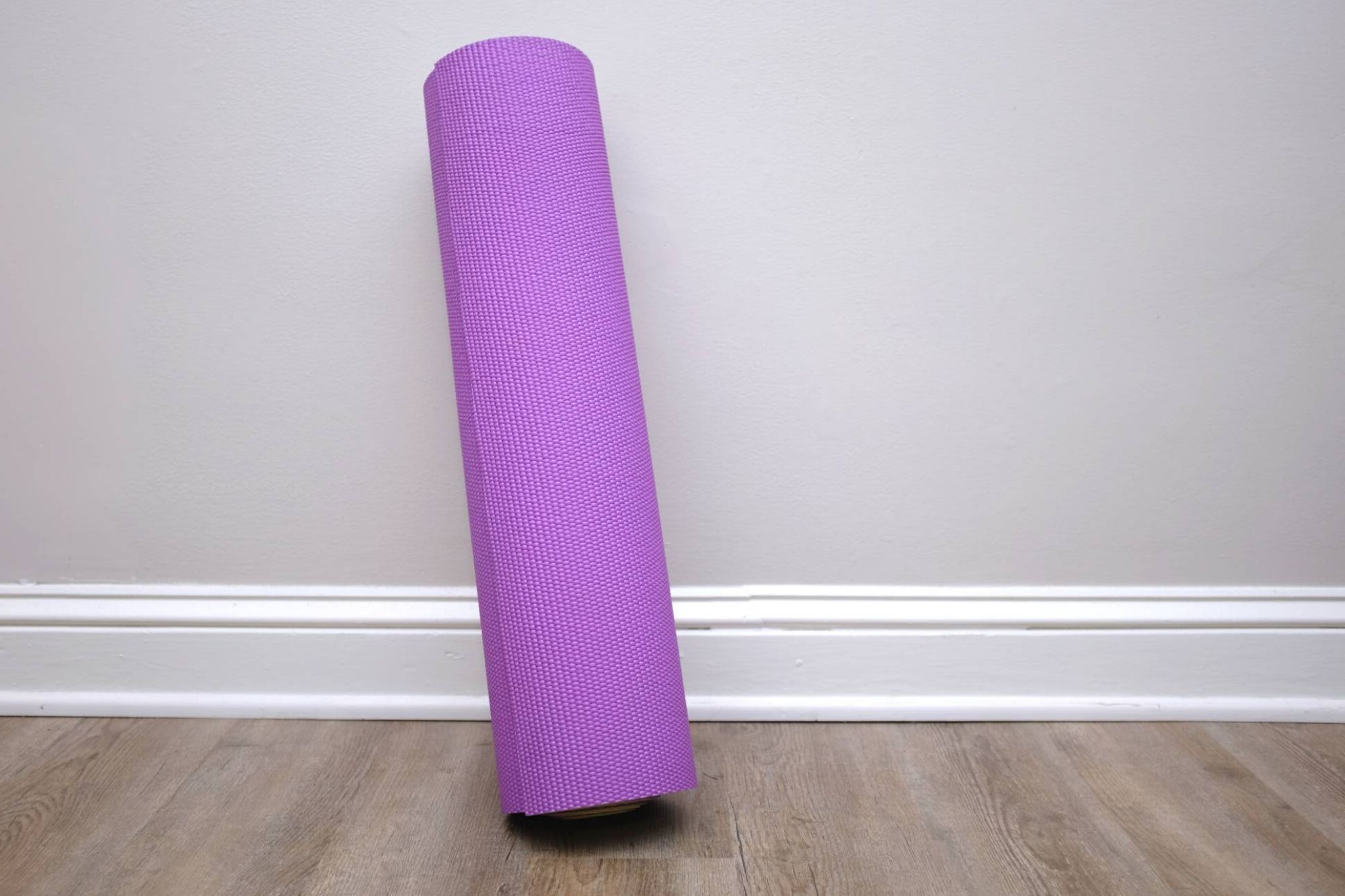 a purple yoga mat rolled up and leaning against a pale grey wall