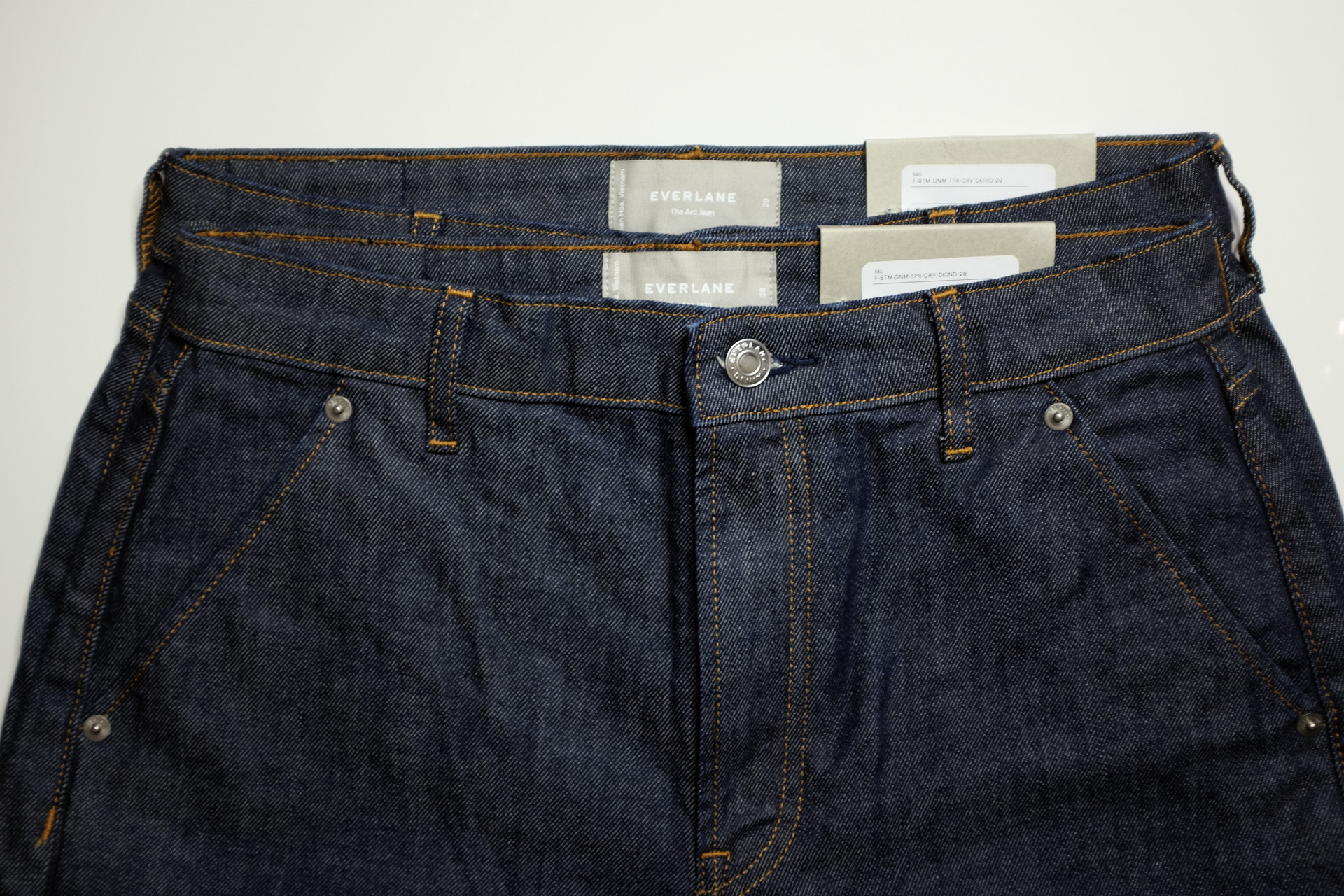 Two pairs of jeans stacked; the smaller size is barely smaller than the larger size