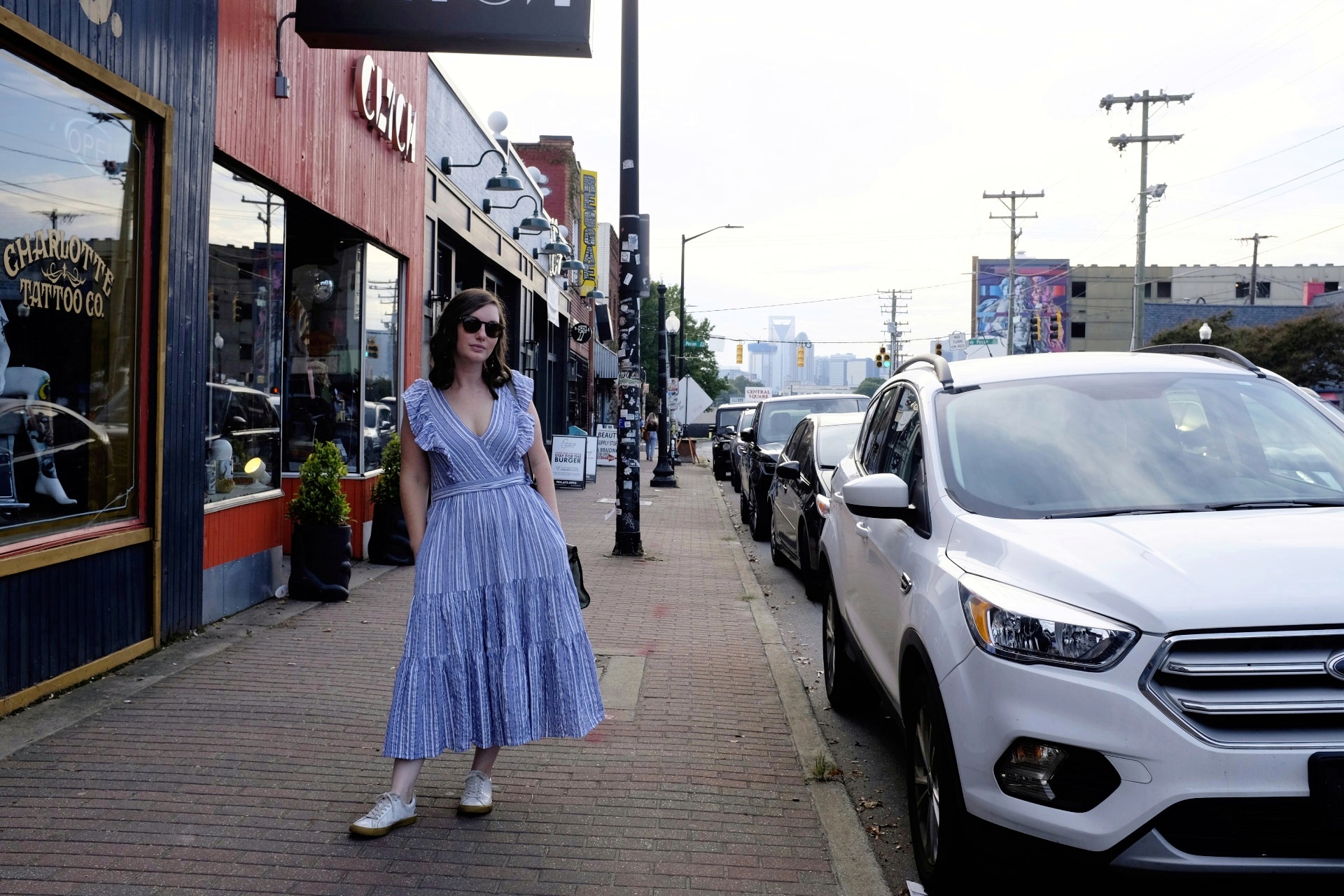 Alyssa stands next to cars on the sidewalk in Plaza Midwood