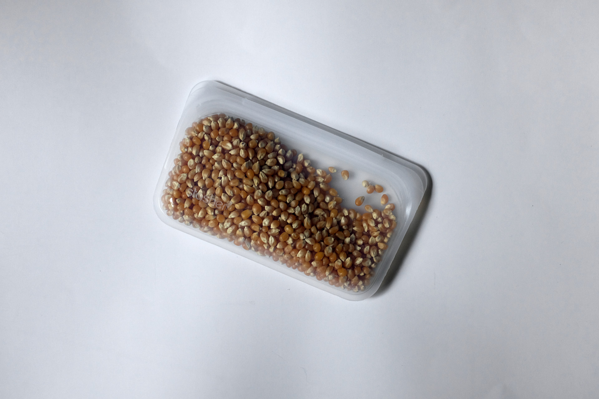 A snack-sized Stasher bag holds popcorn kernels on a white surface