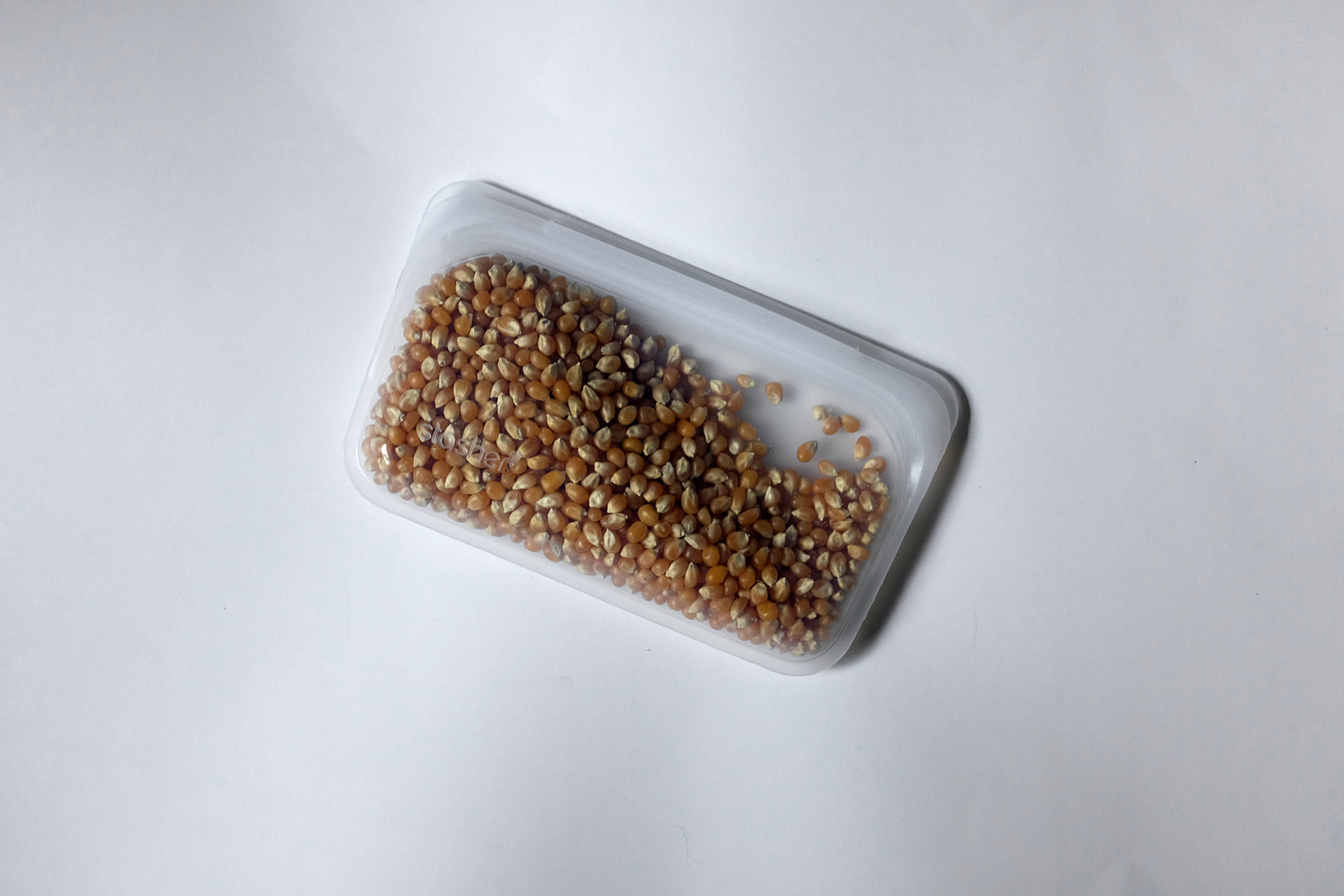 A snack-sized Stasher bag holds popcorn kernels on a white surface
