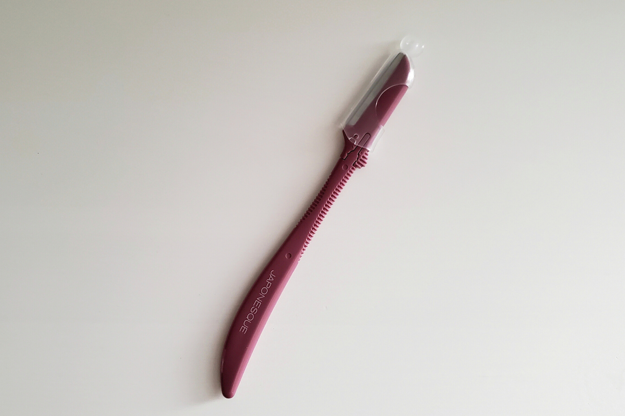 A small magenta handle with a single razor blade at the end with a safety cover over it. It reads "Japonesque" on the side.