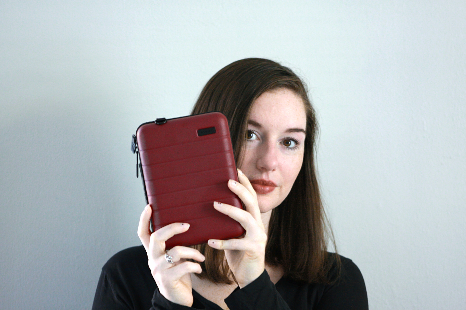 Krystal holds an Away mini suitcase in front of her face. She is peeking out from behind it.