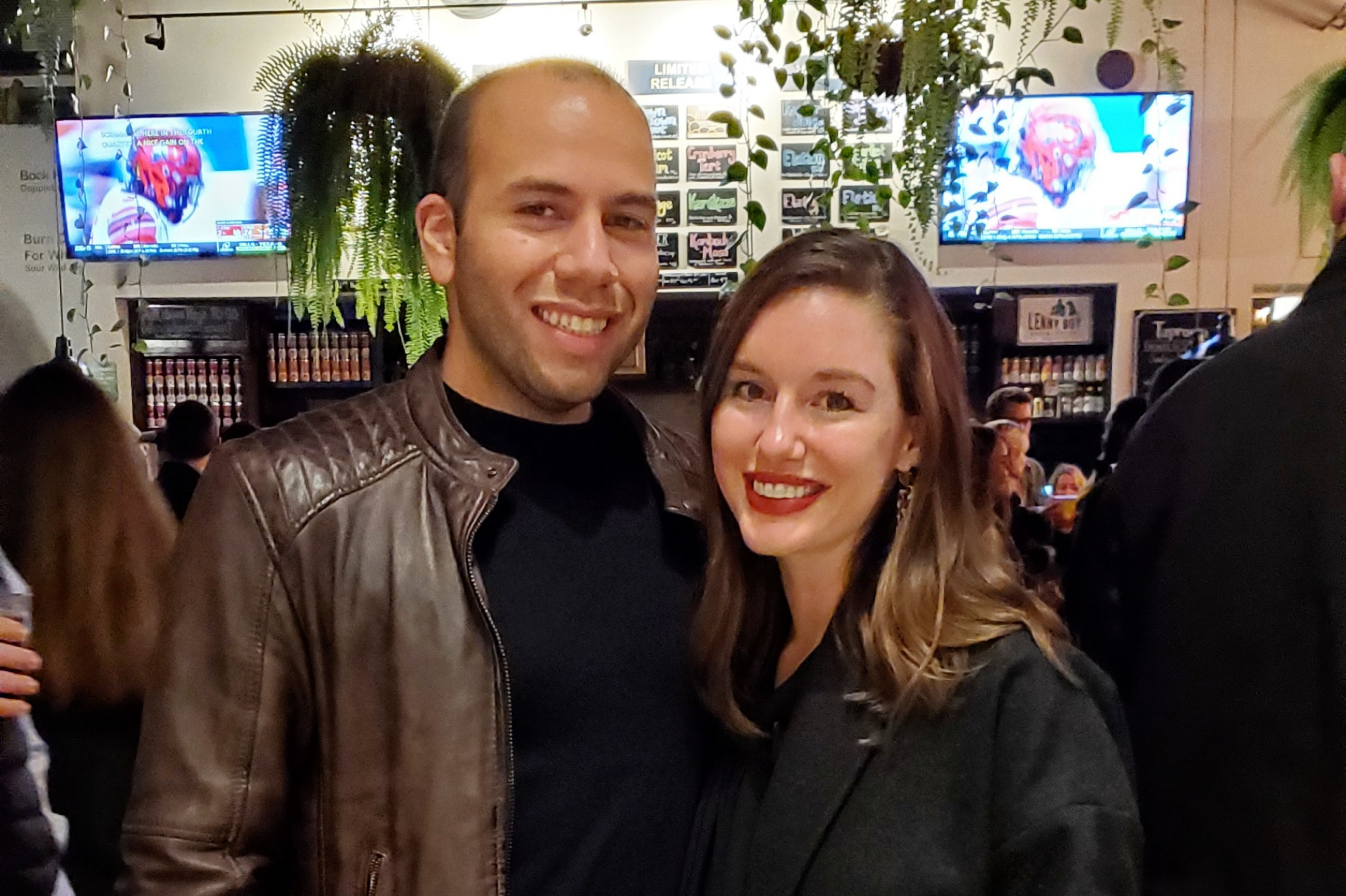 Michael and Alyssa at Lenny Boy on New Years 2020. He is wearing a black shirt and brown leather jacket, she is wearing a grey wool coat over a black top. They are both smiling at the camera, unaware of what 2020 would bring