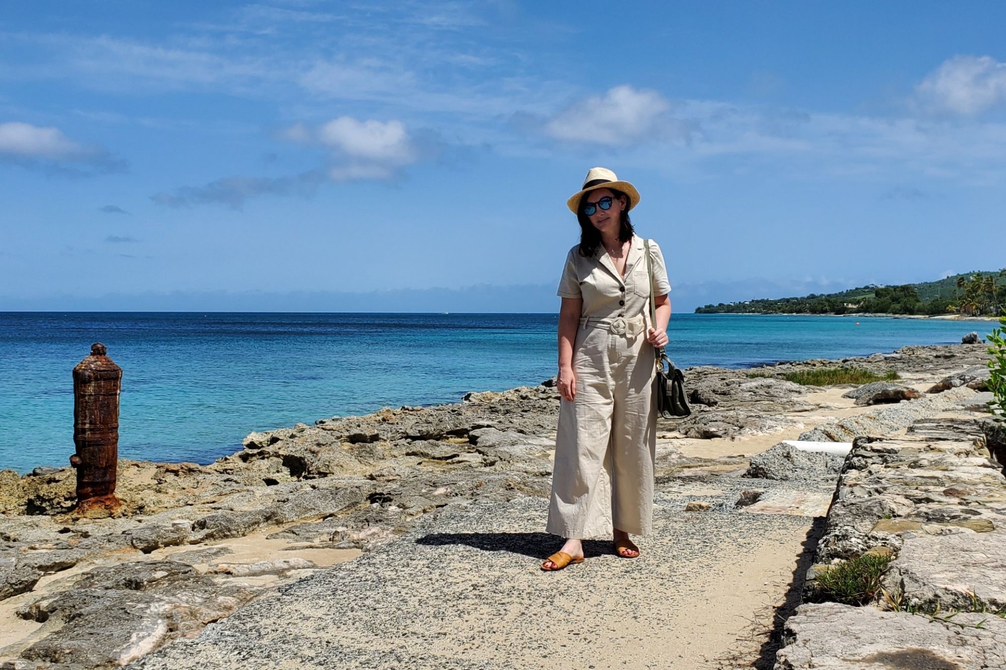 Alyssa is walking along the paved shore in Frederiksted, St. Croix. She is wearing a tan jumpsuit and a Panama hat