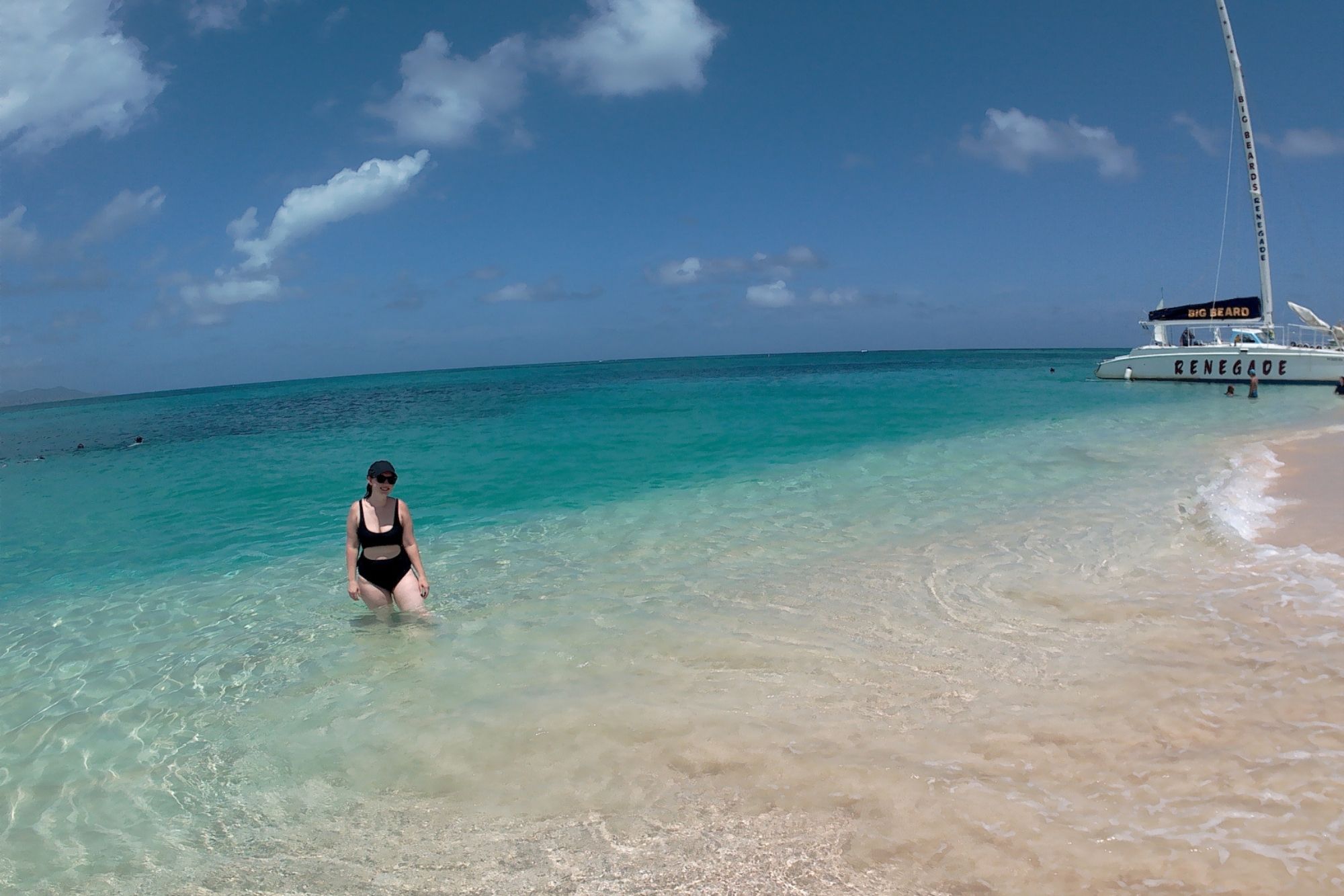 Alyssa stands in the green waters of turtle beach; to the right is a catamaran