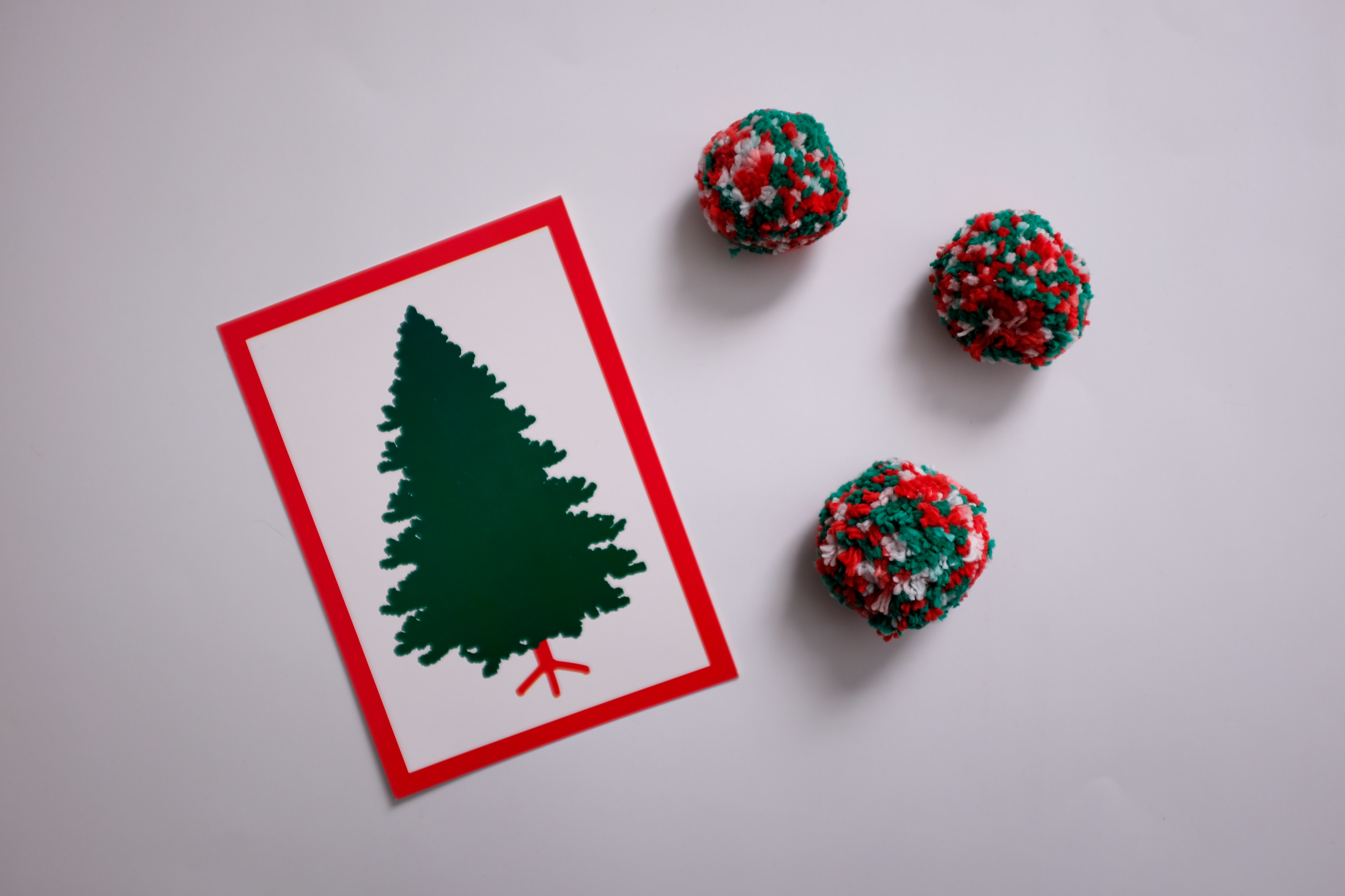 A card with a tree on it with a red border, and three red and green pom poms