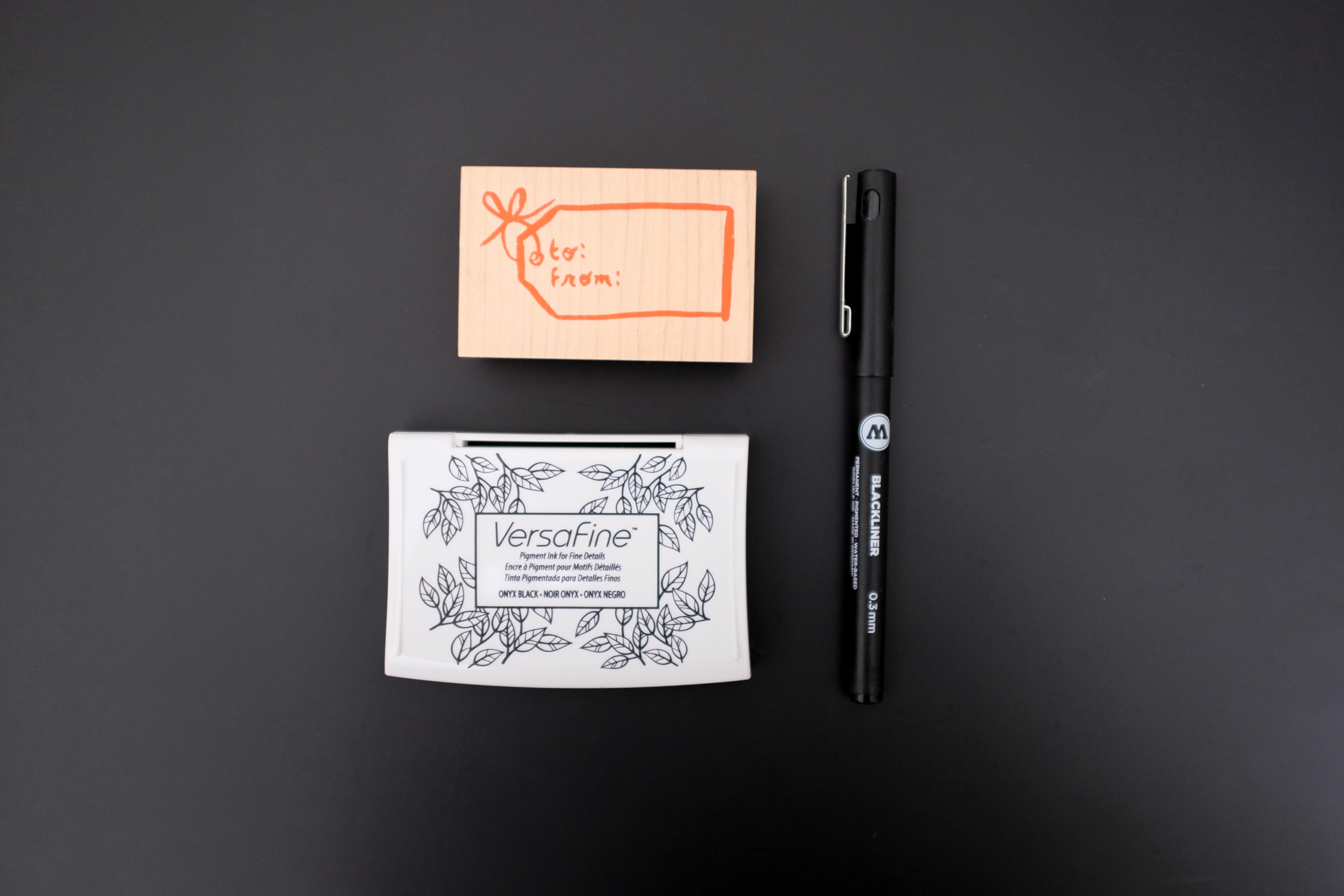 A stamp that reads "to, from", a stamp ink pad, and a pen on a black background