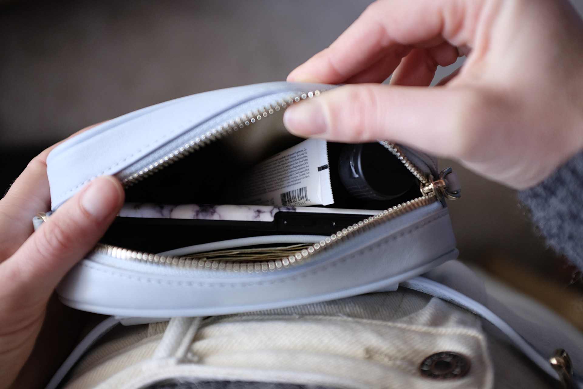 A view from the top of Alyssa opening the belt bag to reveal a phone, lip balm, cash, hand sanitizer, and cards inside.