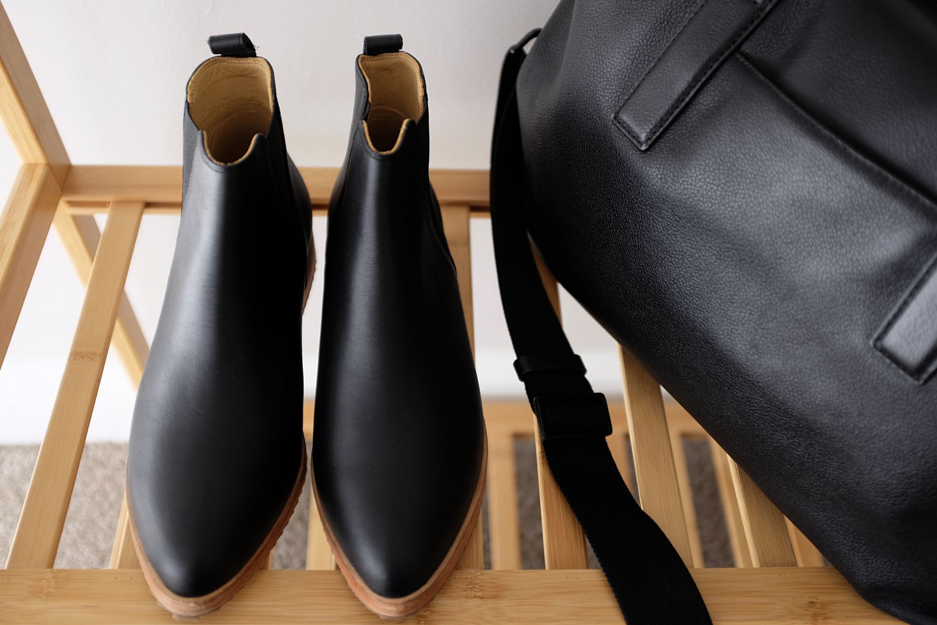 A black pair of boots sits on a garment rack with a leather overnight bag next to it