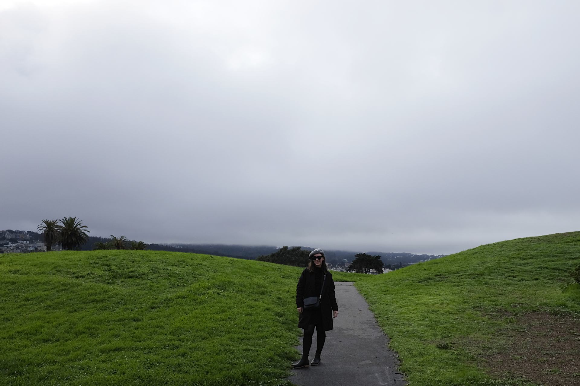 Alyssa standing in a very green field. She is wearing all black and a grey beret