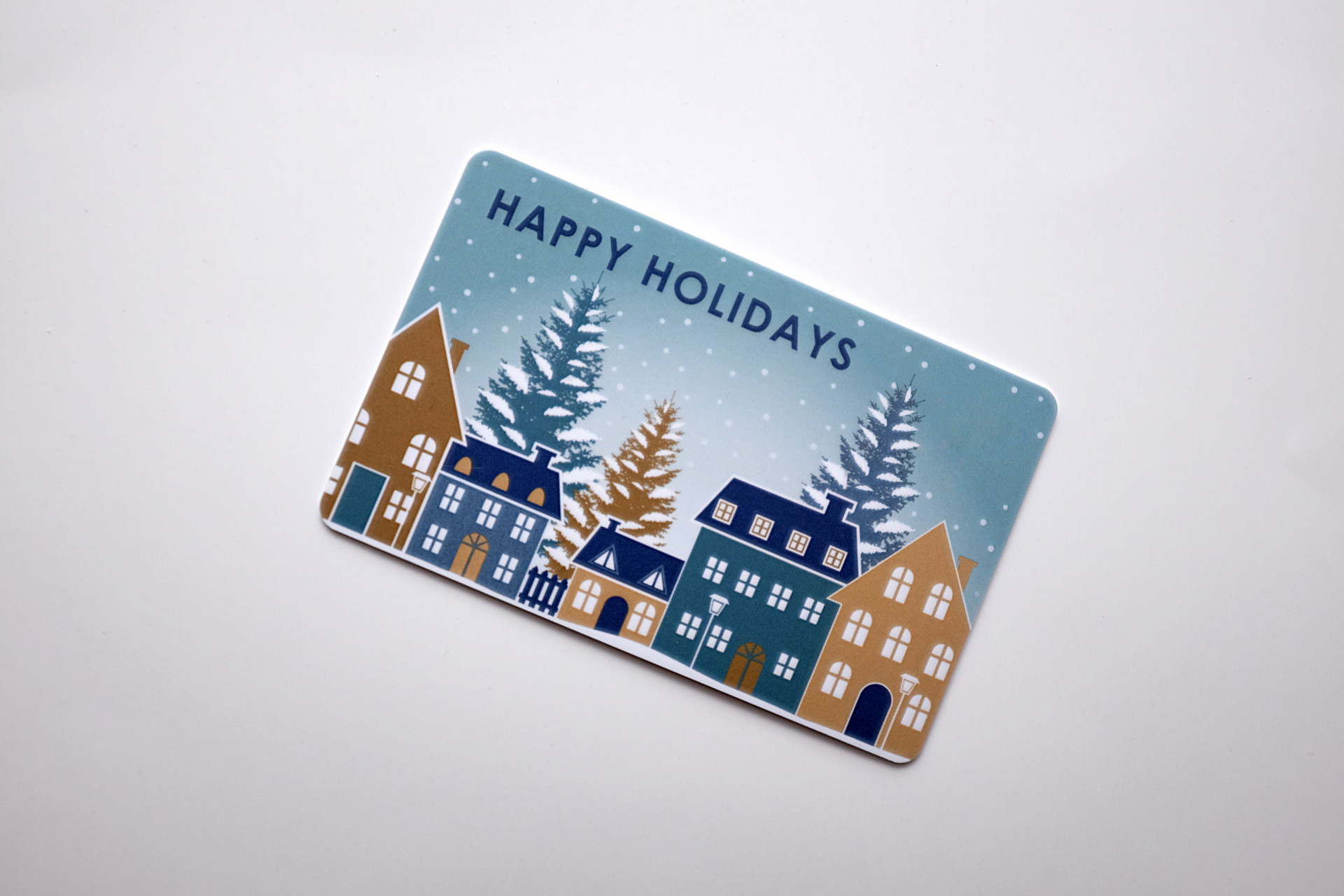 Gift card on a white background that reads "HAPPY HOLIDAYS" and features a winter city scene with buildings and trees and snow