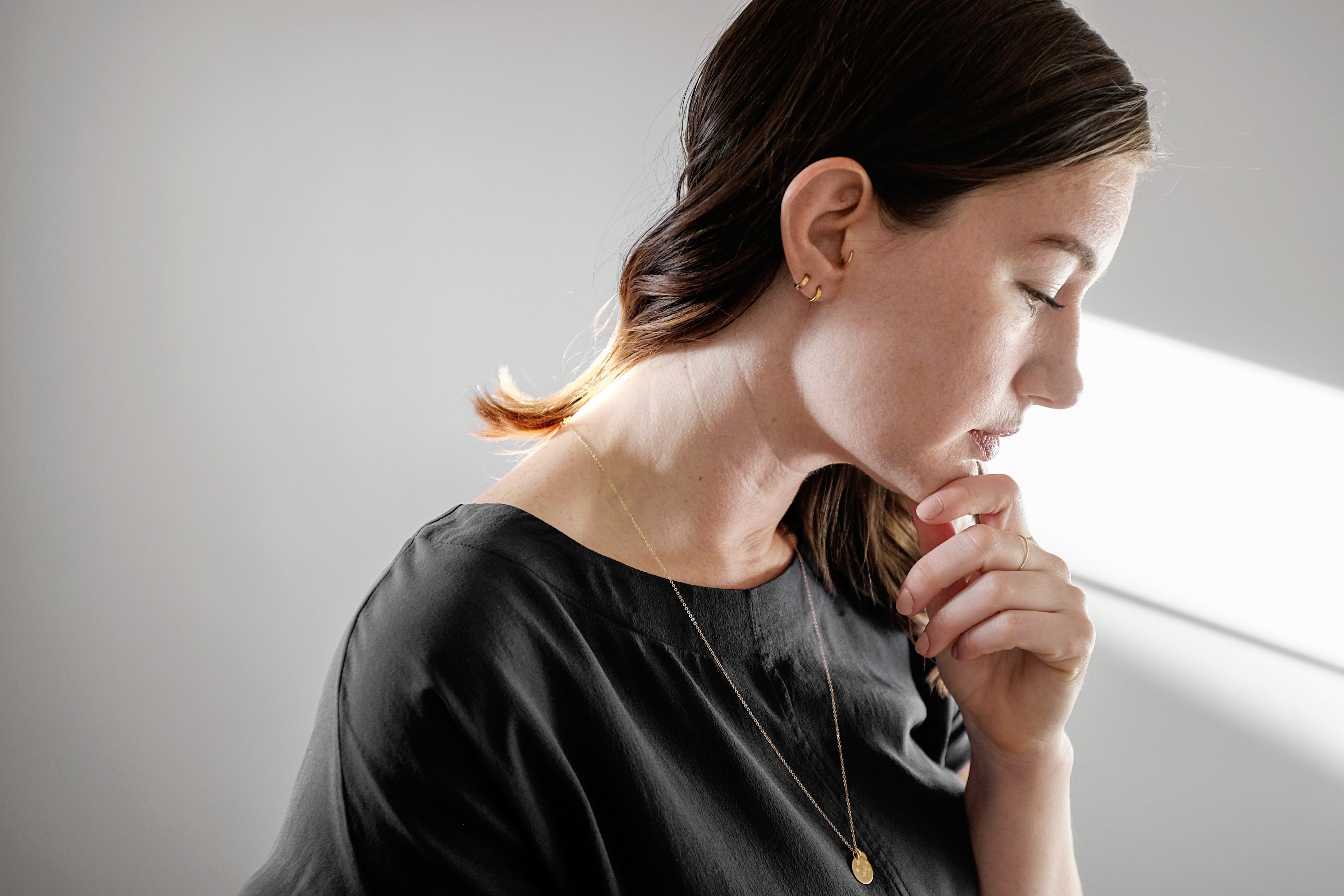 Alyssa holds her chin in her hand - and she is wearing two hoop earrings, a necklace, and a dainty ring