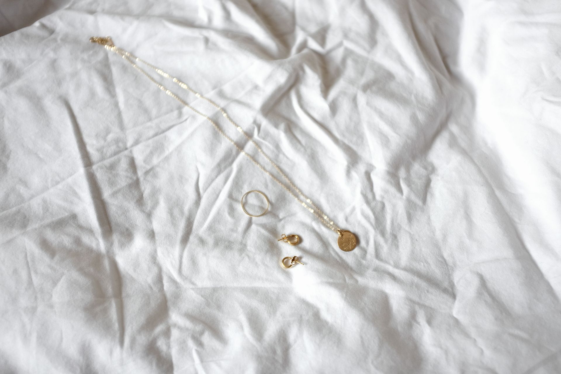 A gold necklace, ring, and pair of earrings sit on a white sheet