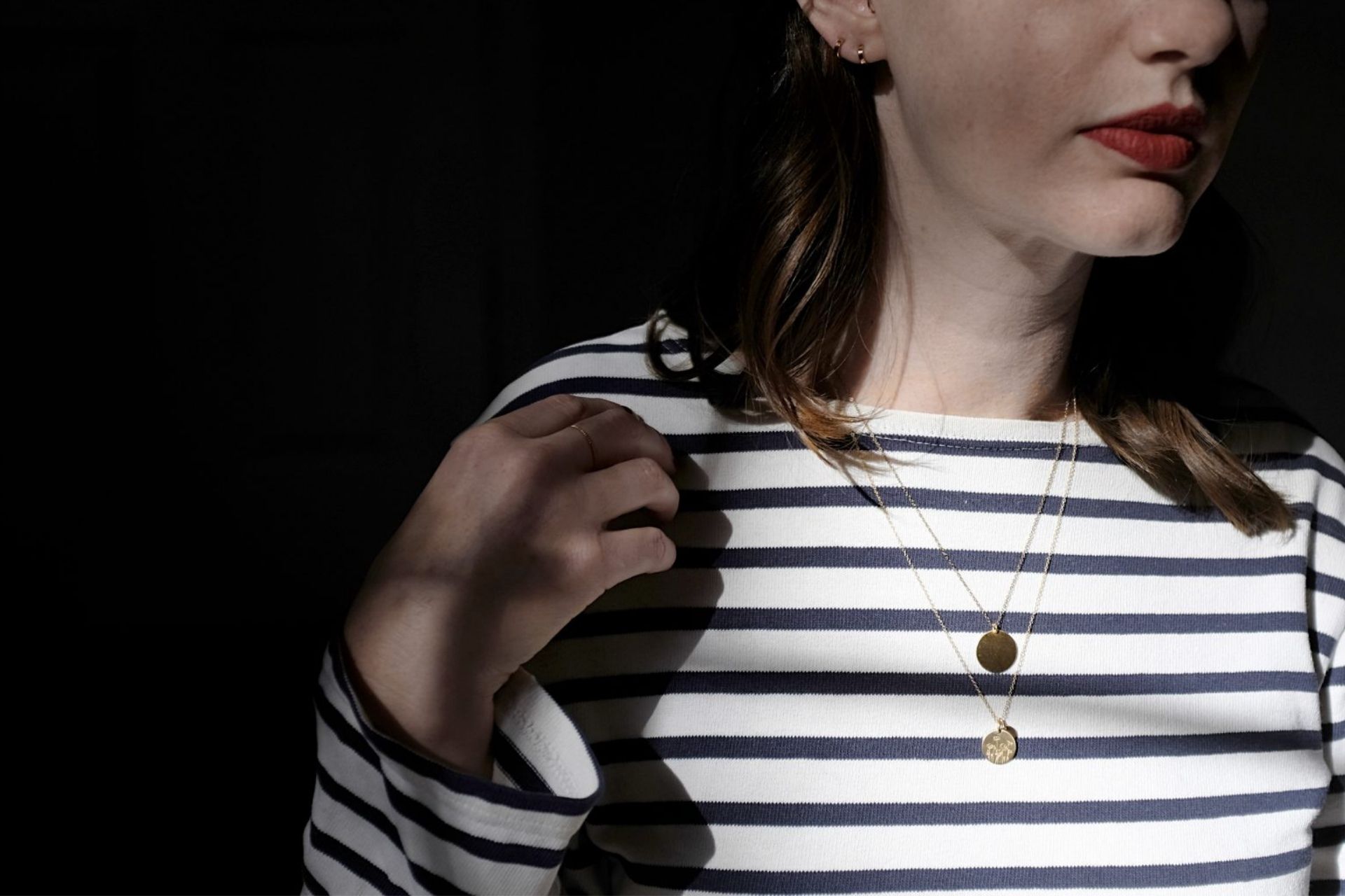 Alyssa is wearing two necklaces, two earrings, and a ring. She is wearing a striped tee and red lipstick, and the image is closely cropped