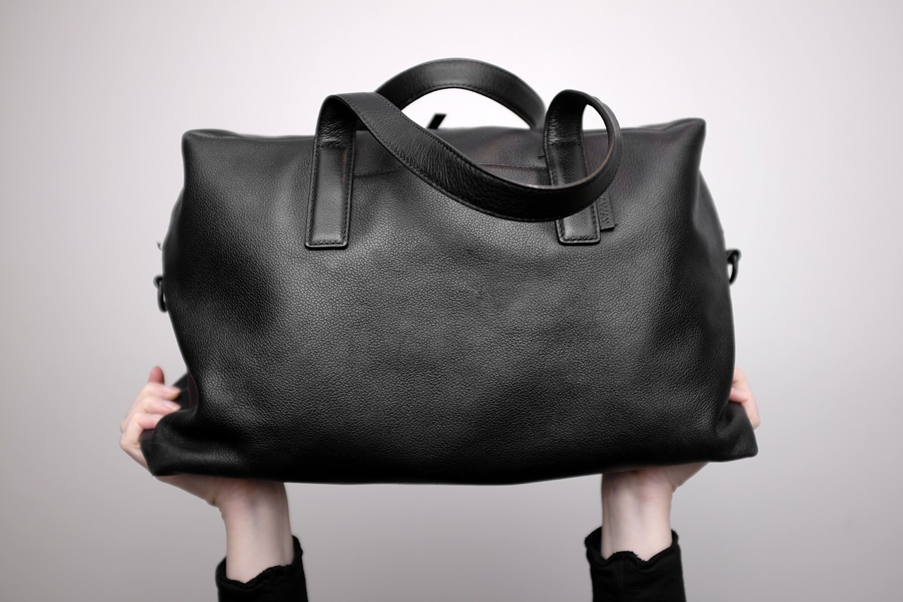 A pair of hands hoist the leather bag in the air