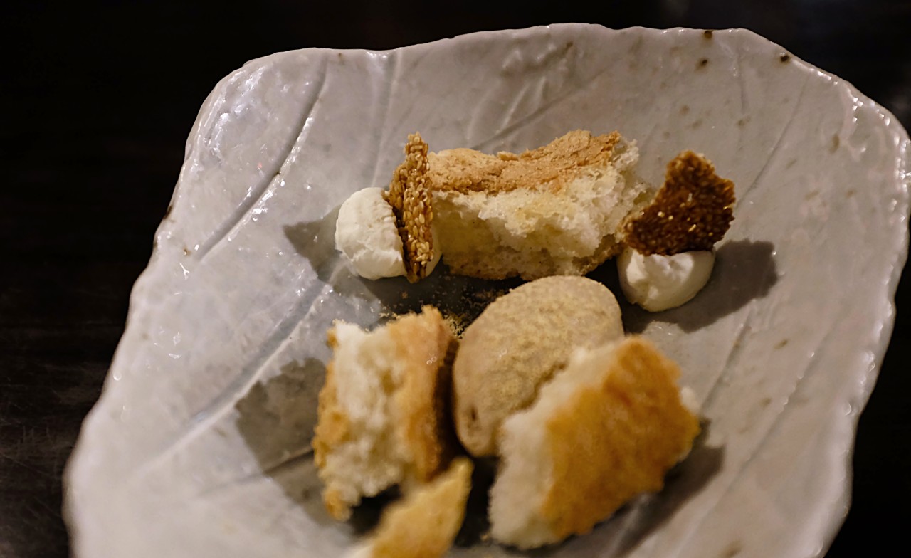 A cream colored platter topped with bits of white cake, cream cheese, and sesame seed brittle