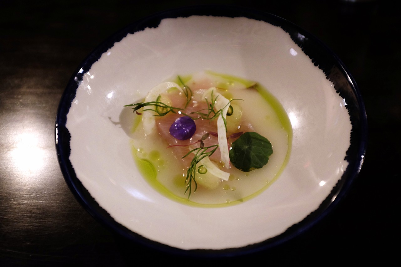 A bowl of raw fish with pieces of apple, fennel, microgreens, and nasturtium