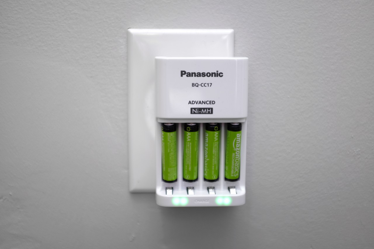 A set of four AAA batteries recharging in a case plugged into the wall