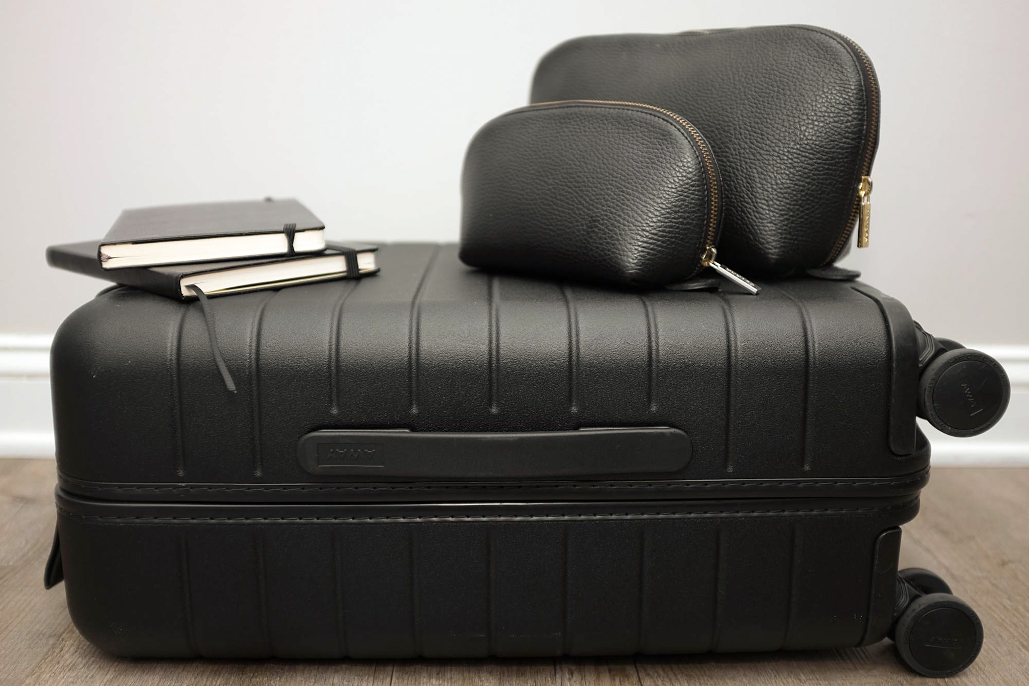 The Leather Travel Set from Cuyana sits on top of a black Away suitcase, and there are two journals next to the travel set