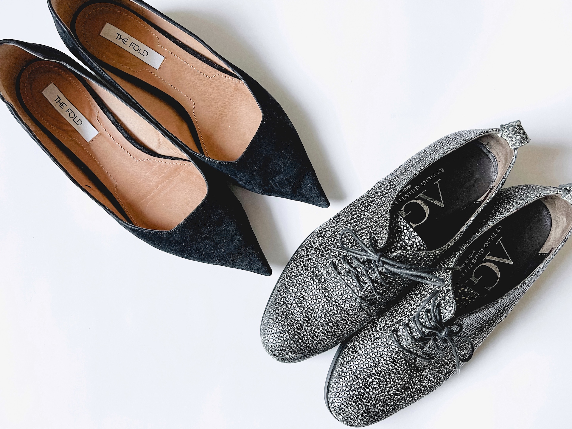 Two pairs of shoes placed at a diagonal angle on a white background. The left pair is a pointy black flat from The Fold, and the right is a pair of snake-like oxfords rom AGL