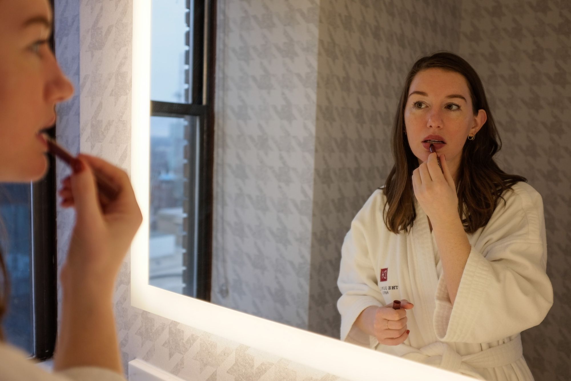 Alyssa applies lipstick while wearing the hotel robe