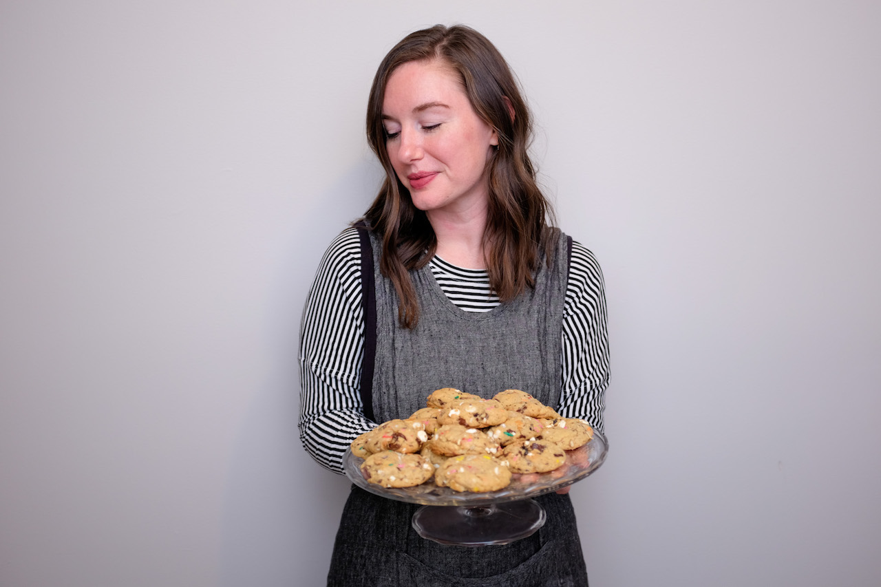 Alyssa stands in front of a grey wall with a clear glass platter of cookies