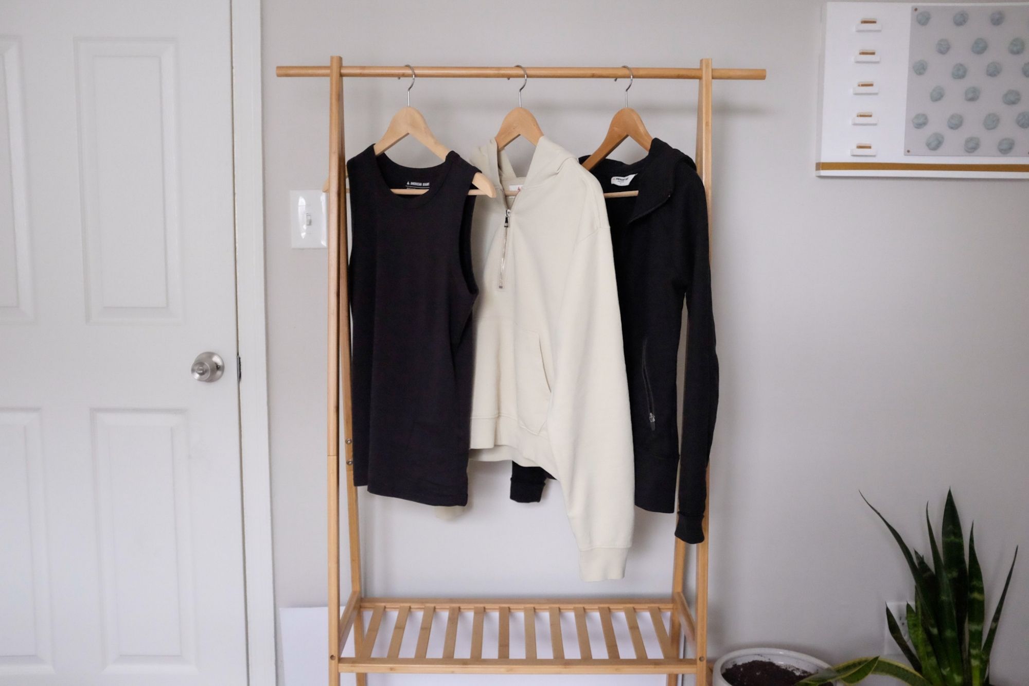 A black tank, cream hoodie, and black hoodie all hang on a bamboo coat rack