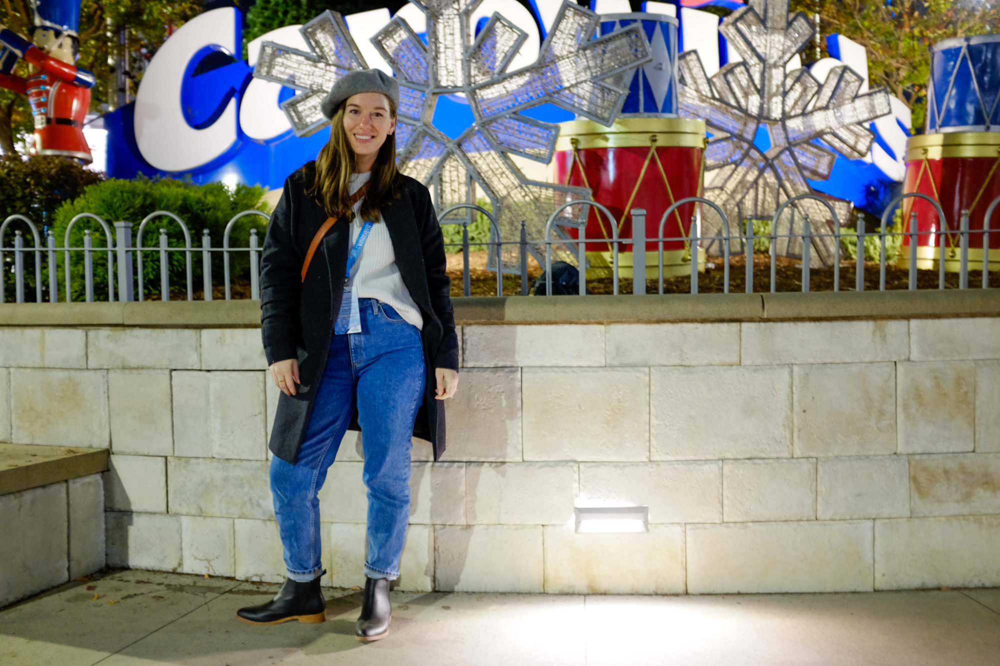 Alyssa wears a sweater, jeans, boots, and beret in front of the Carowinds sign