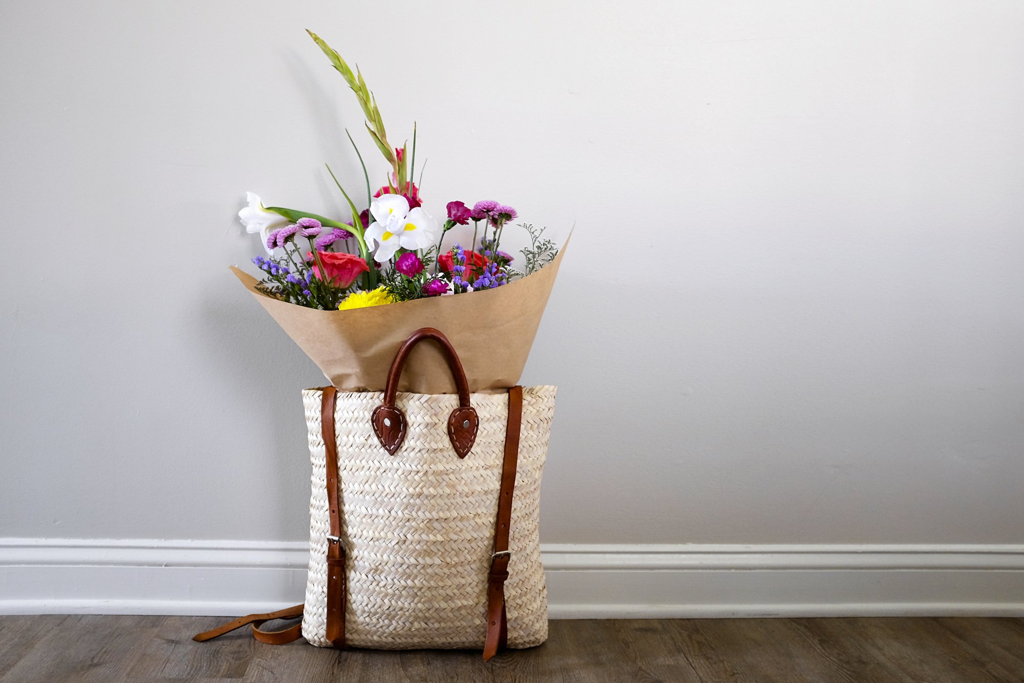 A bouquet of flowers sits in a straw backpack