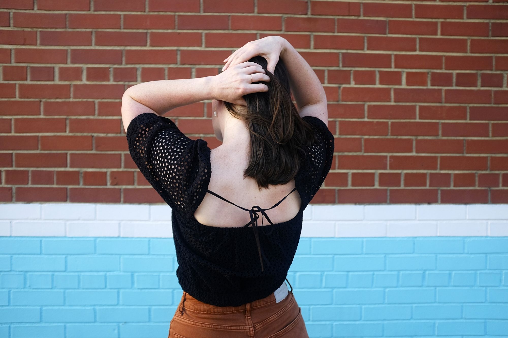 Alyssa wears an eyelet top with orange-brown denim