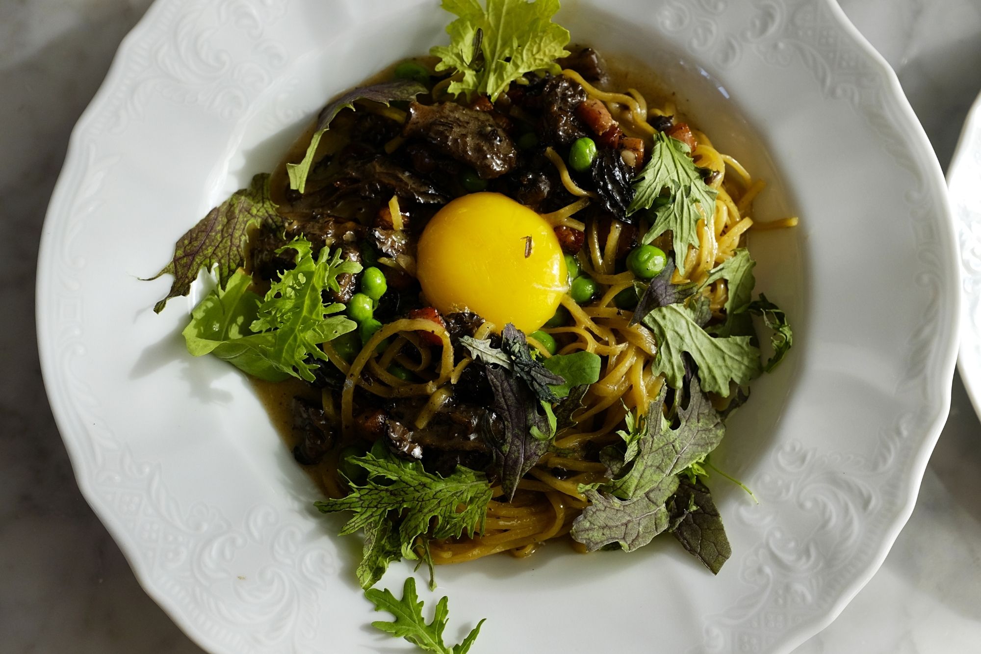 A bowl of tagliolini with greens and an egg yolk