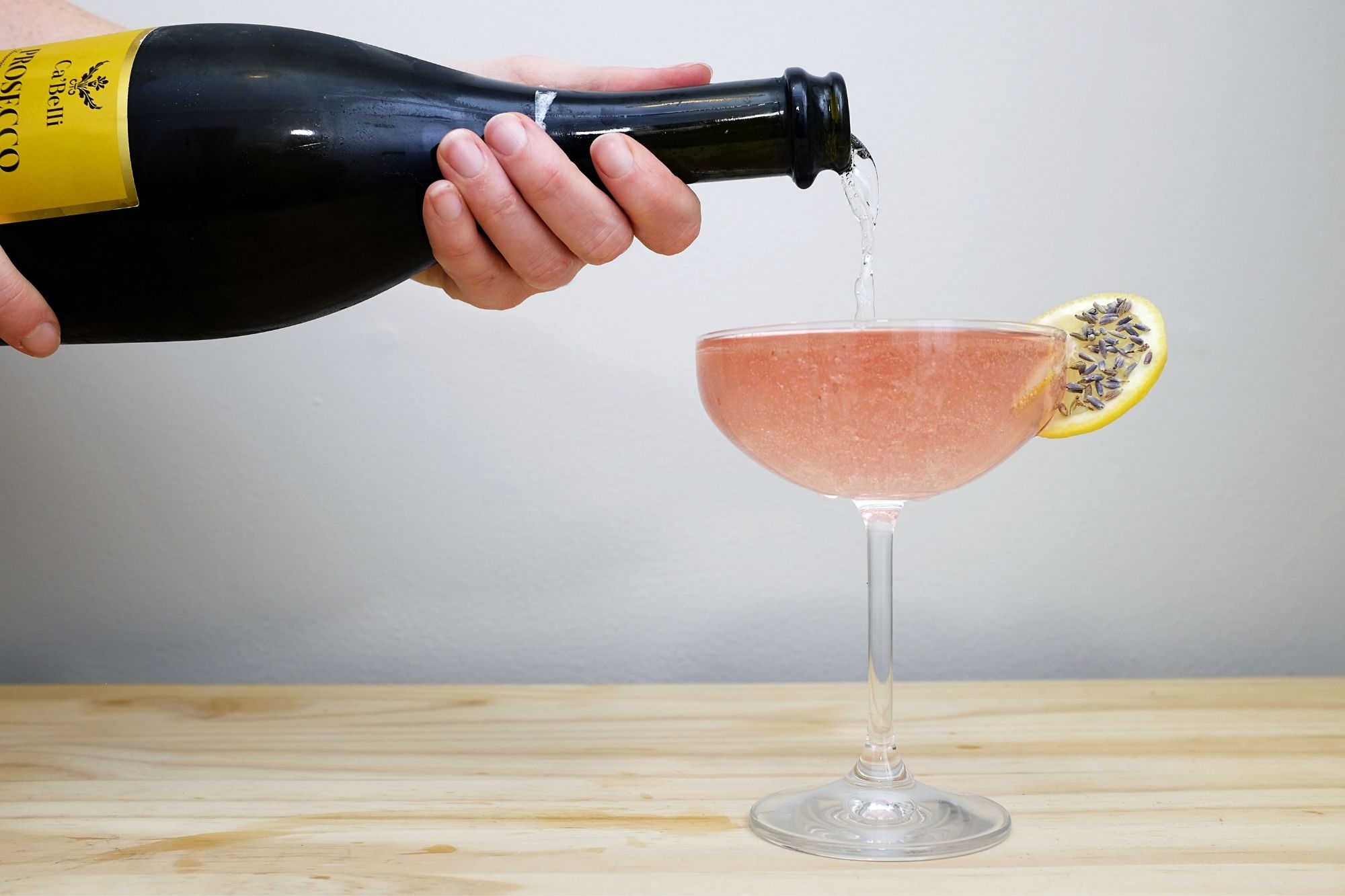 a hand pours prosecco in a coupe glass