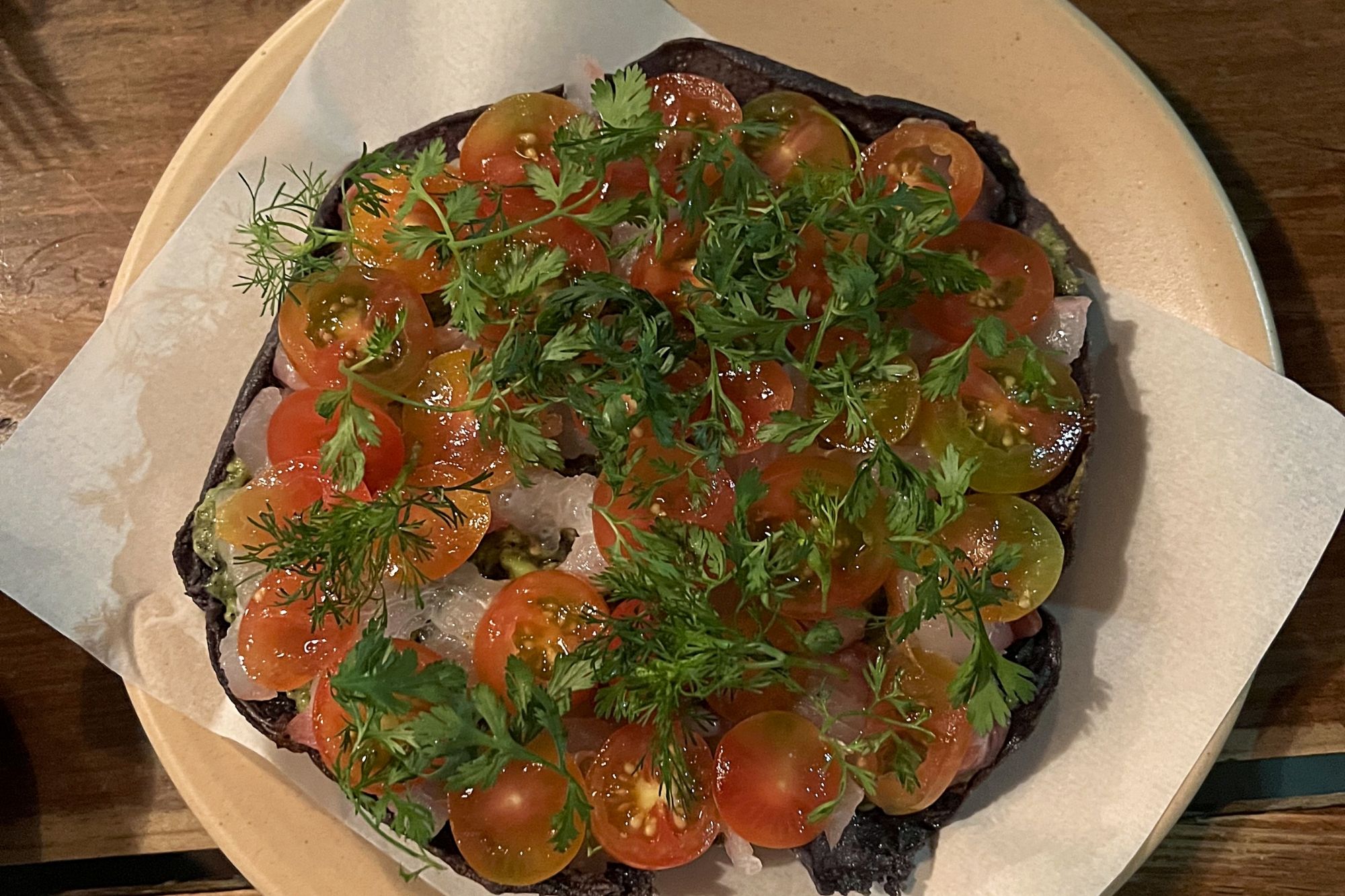 a large tostada topped with tomatoes, fish, and herbs