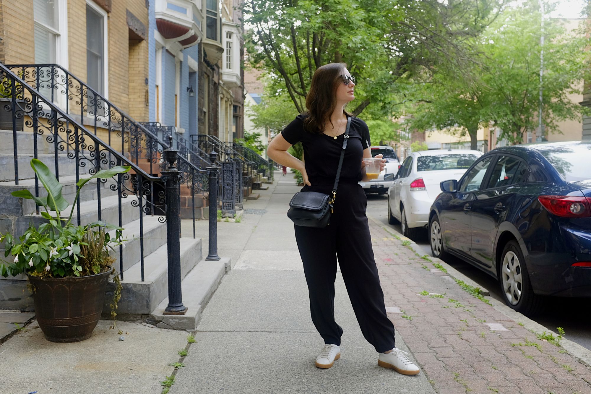 Alyssa stands with a coffee wearing a black tee and black joggers