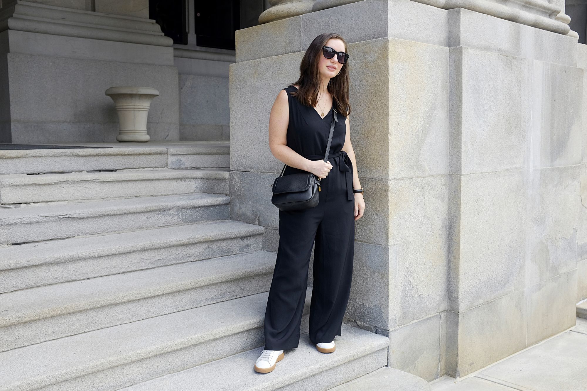 Alyssa stands by the NY State Capitol Building in a black jumpsuit