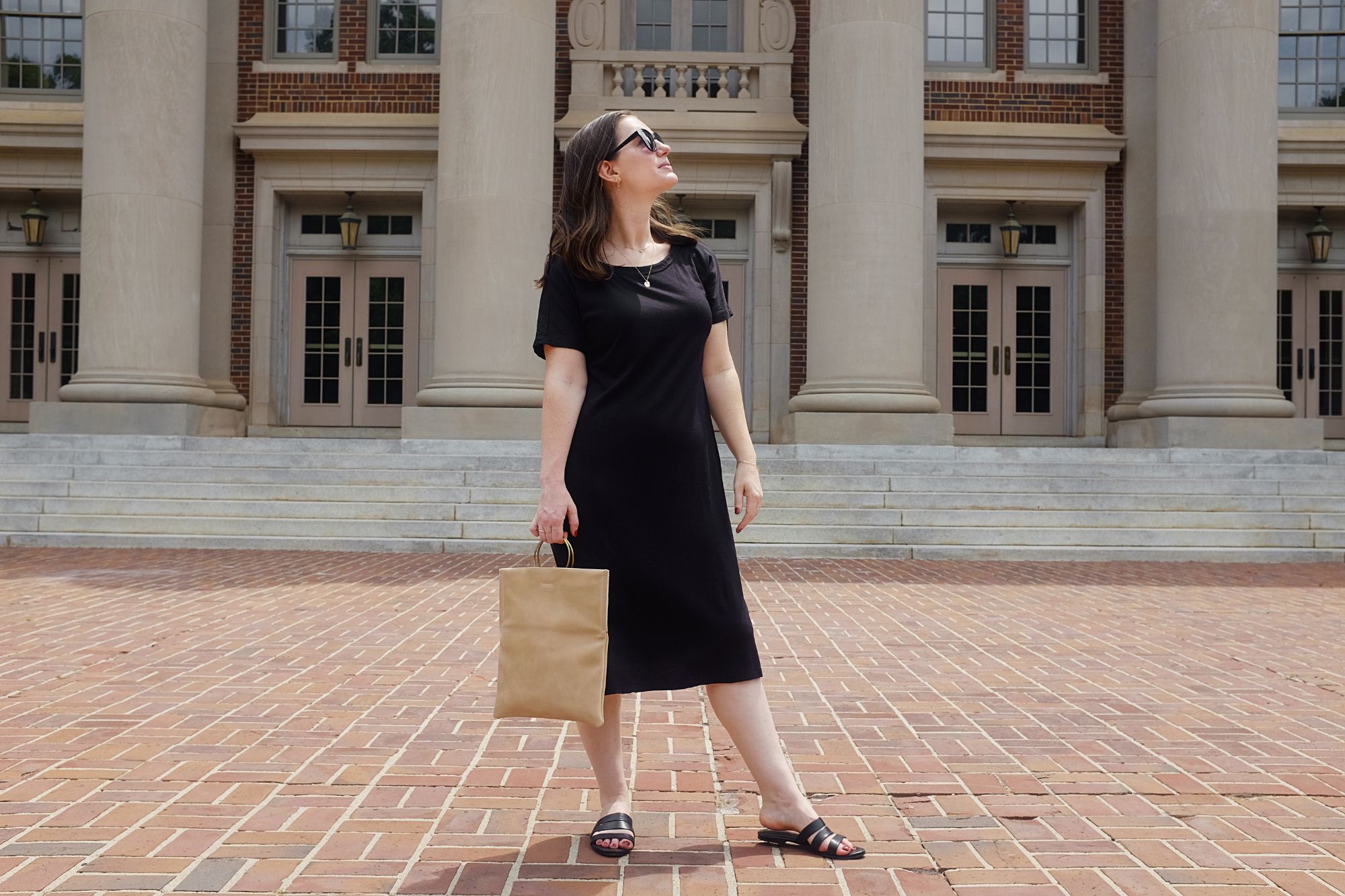 Alyssa stands in front of a column building wearing a black dress and carrying a tan tote