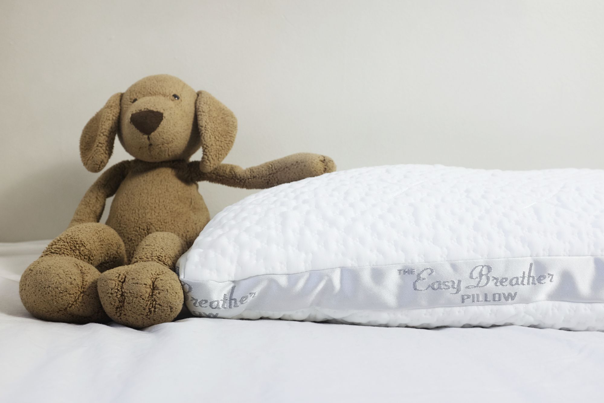 A stuffed animal (he's a doggie and his name is Hank) sits next to the Easy Breather Pillow from Nest Bedding