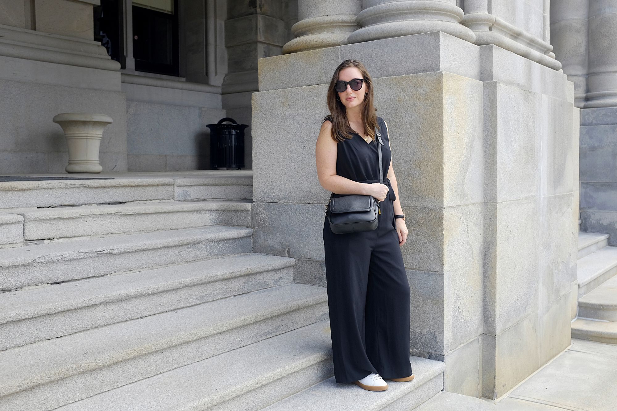 Alyssa stands by the NY State Capitol Building in a black jumpsuit