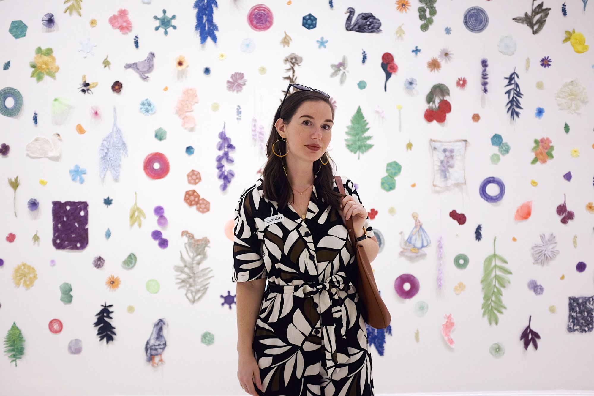 Alyssa wears a botanical jumpsuit and stands in front of an art display
