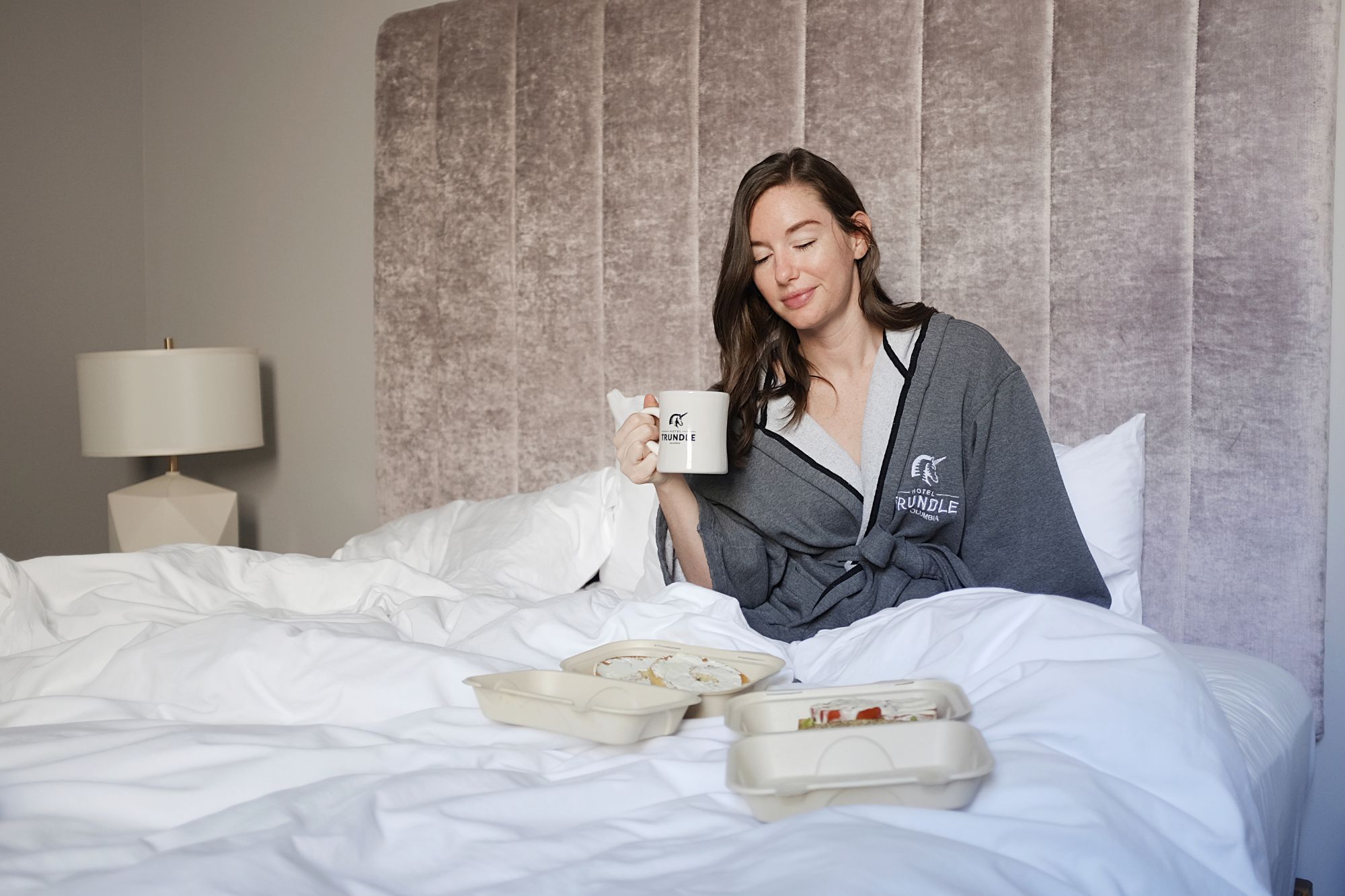 Alyssa sits in bed at the Hotel Trundle with coffee and breakfast