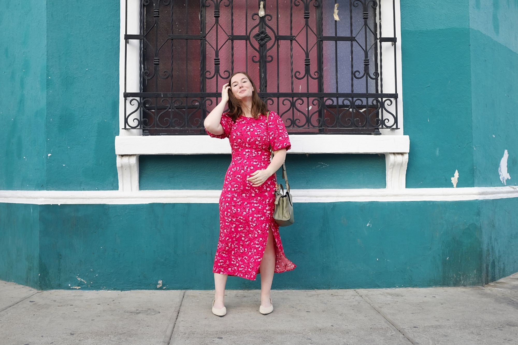 Alyssa wears a red dress and stands in front of a teal wall